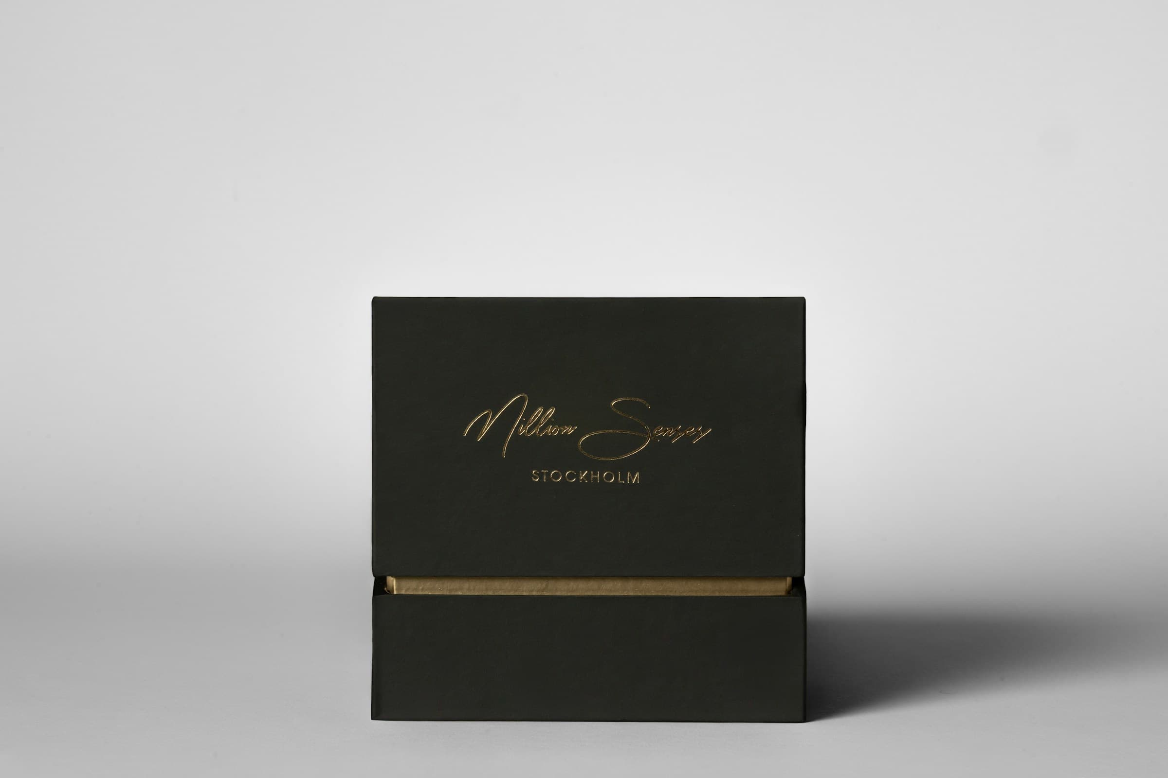 A black rigid lift-off box stamped with a fine gold-foil signature script — the kind of small, sharp foil mark that a hot-foil press is built to deliver